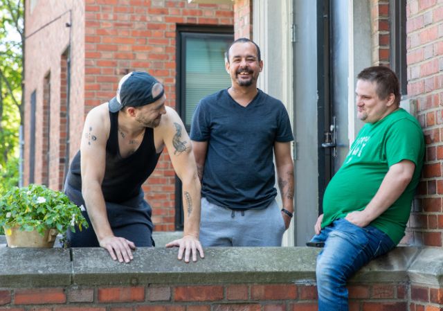 three men hanging out outside on a front porch